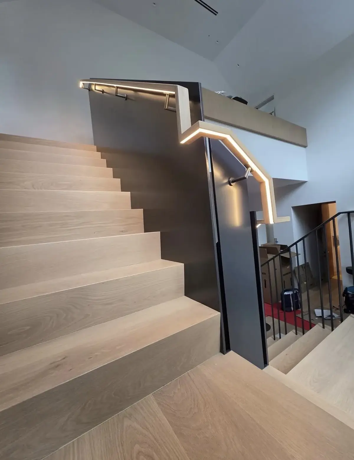 Light oak staircase with a dark guard panel and an LED strip set into the handrail, wrapping around the landing above